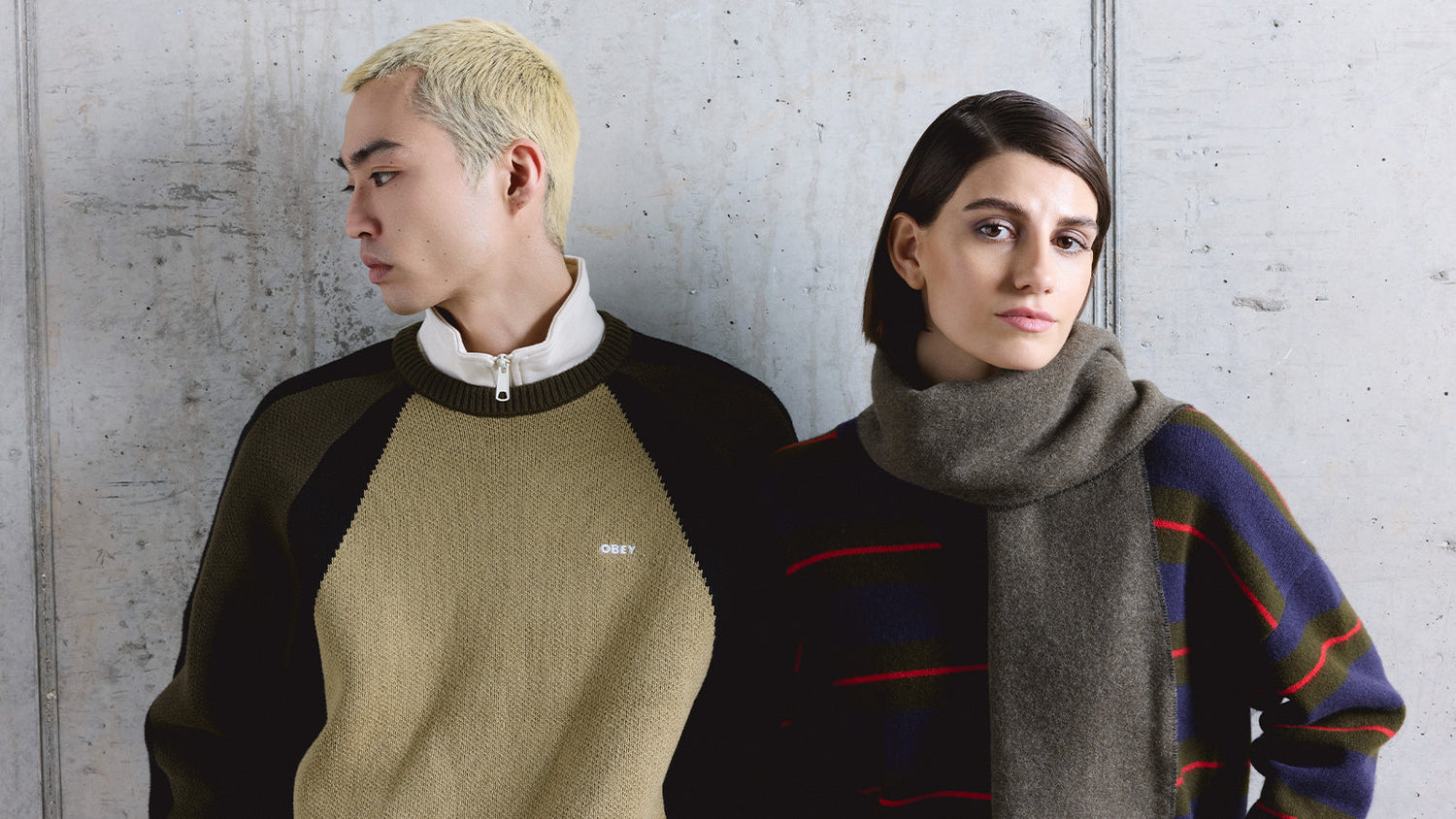 Man and women stood in front of grey textured wall wearing winter knitwear