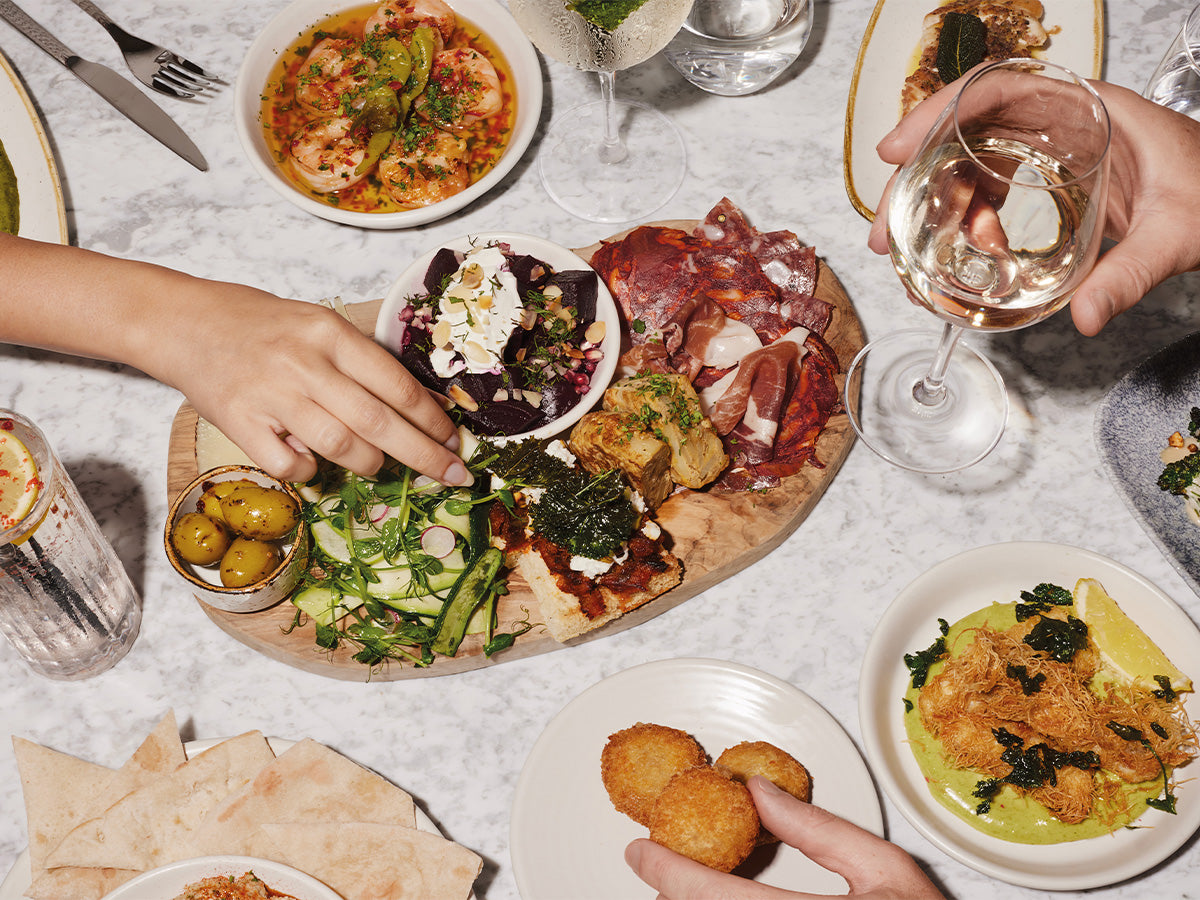 Diverse food platter with various dishes on a table, including a hand reaching for a salad.