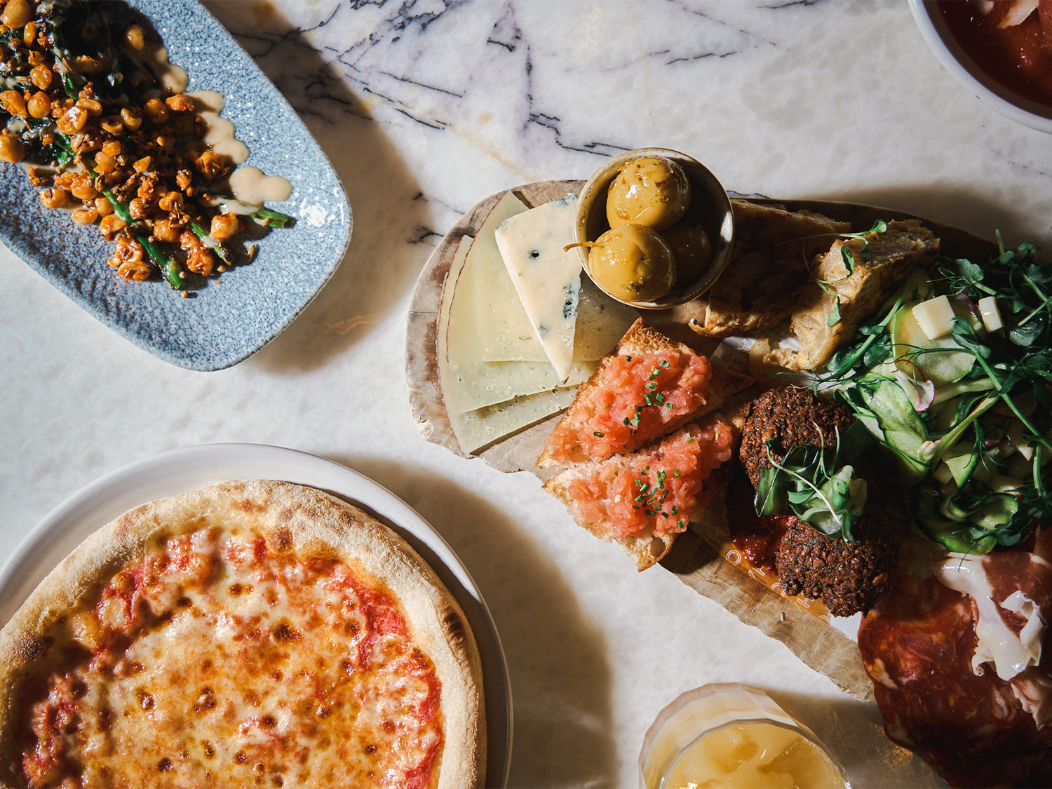 Assorted dishes for Fenwick NE1 Restaurant Week including a pizza, falafel, and salad on a marble surface.