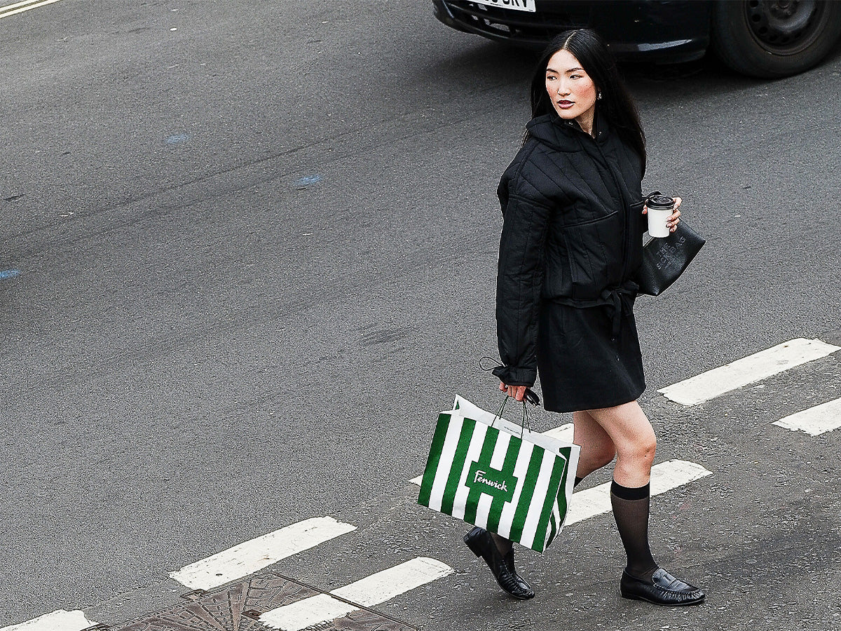 Woman in black coat holding a striped bag and coffee cup on a street