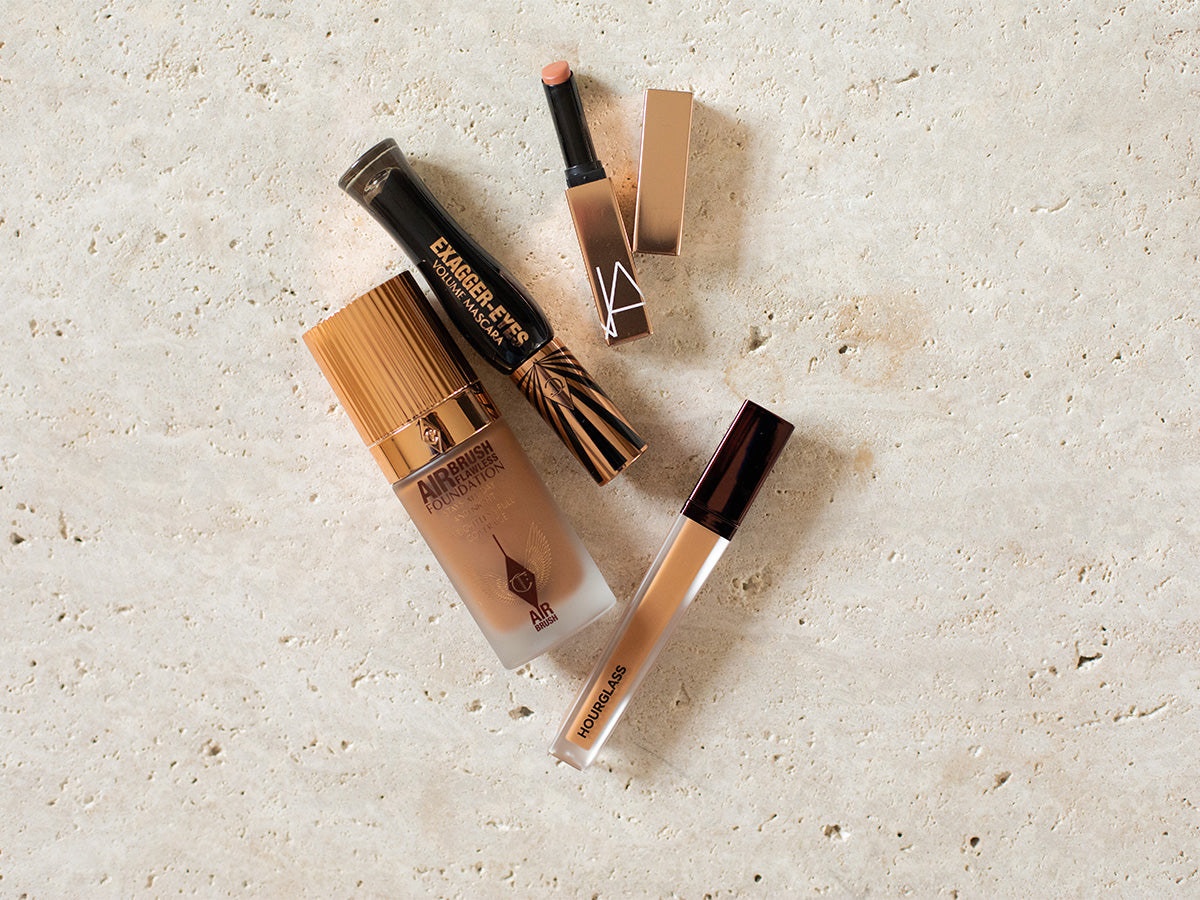 Makeup products including a Hourglass concealer and two lip products on a textured beige surface