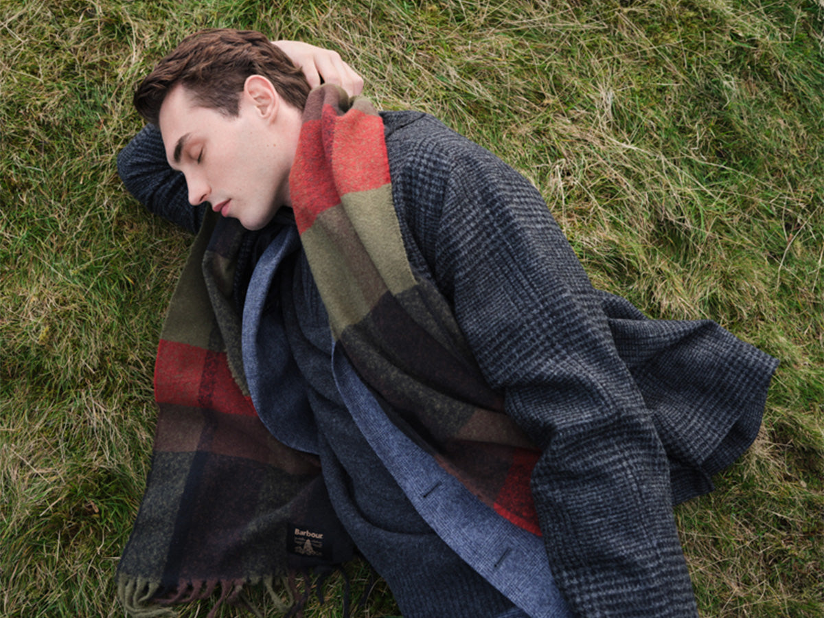 Man laying on grass wearing winter clothes including a tartan Barbour scarf