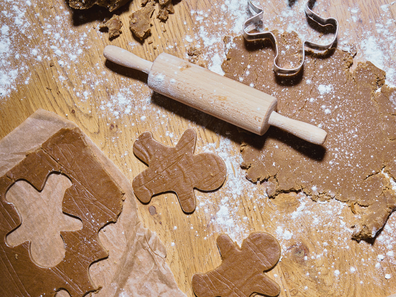 Baking scene with gingerbread cookies, rolling pin, and cookie cutters on a wooden surface.